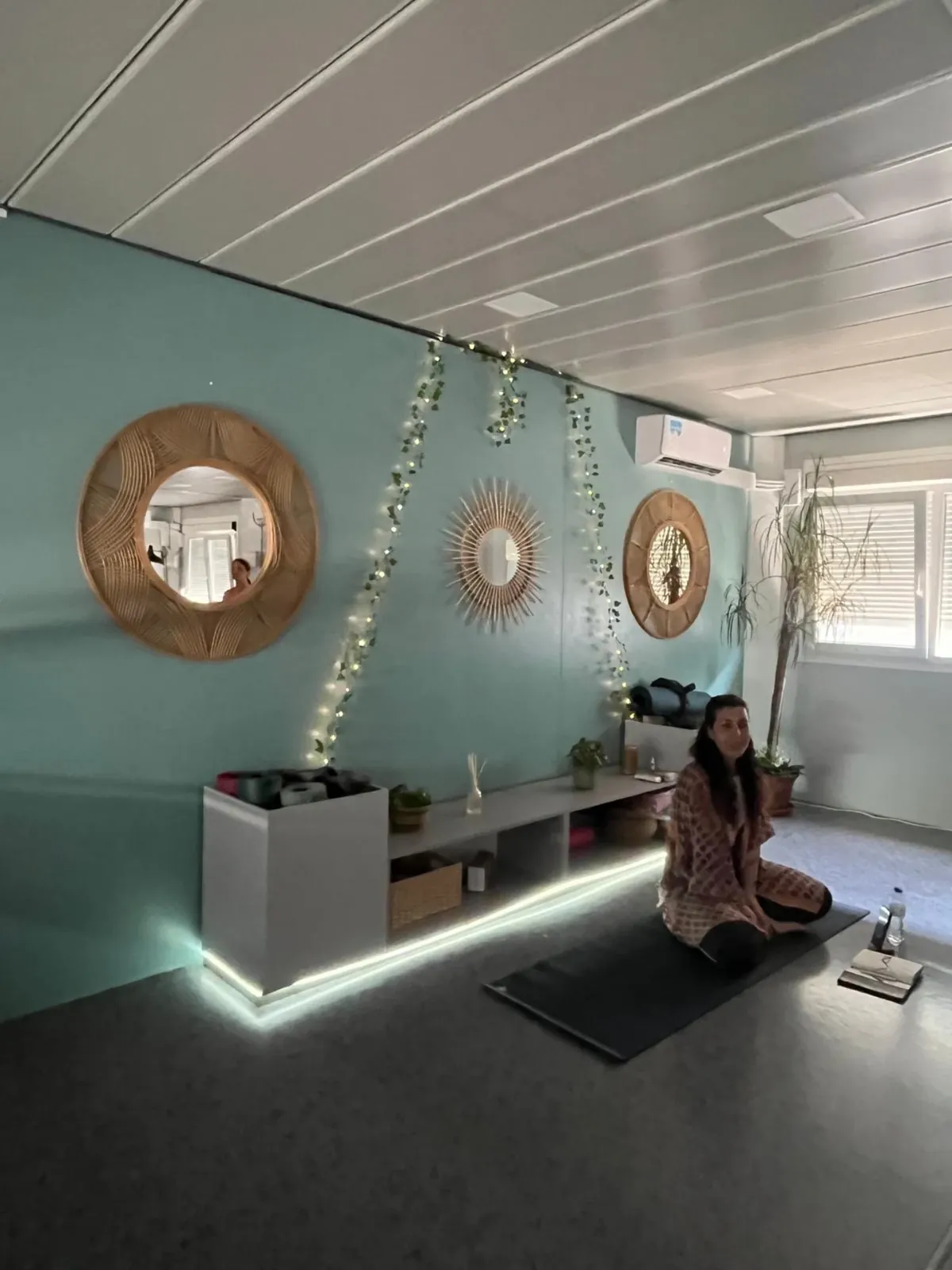 Professora a meditar sentada na sala do HomYoga, com espelhos dourados e luzes na parede